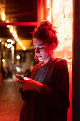 Attraktive stilvolle Dame mit Smartphone in der Nähe von Neonlichtern - ADSF06525