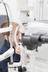 Optikerin testet die Augen eines Jungen mit optometrischen Geräten - ADSF06530