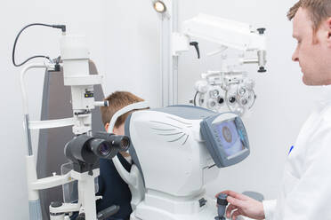 Optikerin testet die Augen eines Jungen mit optometrischen Geräten - ADSF06533