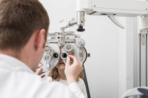 Optician testing a girl's eyes with optometry devices - ADSF06537