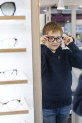 Cute young boy trying on glasses in an eyewear store - ADSF06539