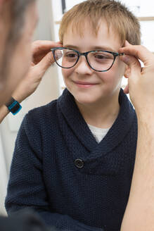 Niedlicher Junge, der in einem Brillengeschäft eine Brille anprobiert - ADSF06541
