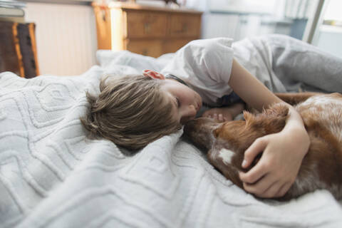 Cute boy cuddling dog on bed stock photo
