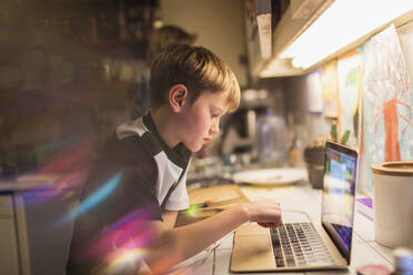 Focused boy doing homework at laptop in kitchen - CAIF28808