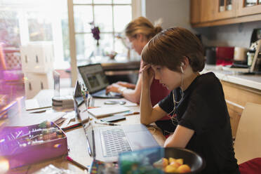 Konzentrierter Junge bei der Hausaufgabenbetreuung am Laptop in der Küche - CAIF28819