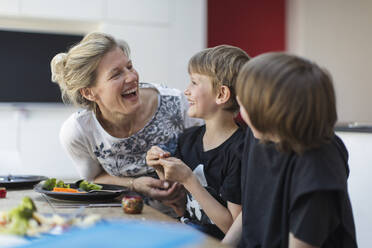 Happy mother and sons eating dinner at table - CAIF28826