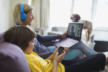 Mutter und Sohn benutzen Laptop und Smartphone auf dem Sofa - CAIF28838