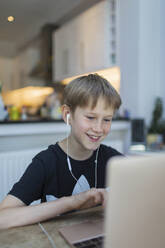 Smiling boy with headphones homeschooling at laptop - CAIF28846