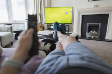 POV Mann auf Sofa mit Fernbedienung schaut Fußballspiel im Fernsehen - CAIF28859