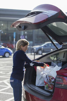 Frau lädt auf einem Parkplatz Lebensmittel in den Kofferraum eines Autos - CAIF28865