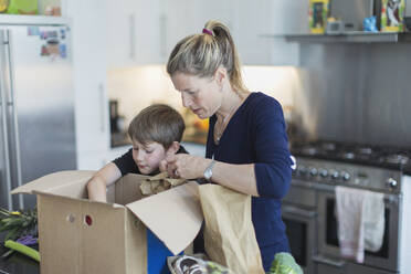 Mother and son unloading produce from box in kitchen - CAIF28871