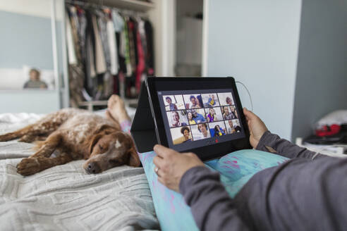 Woman with digital tablet video chatting with friends on bed with dog - CAIF28873