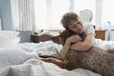 Niedlicher Junge, der seinen Hund auf dem Bett umarmt - CAIF28874