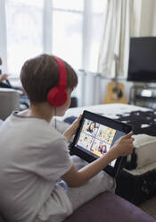 Boy with headphones and digital tablet homeschooling on sofa - CAIF28892