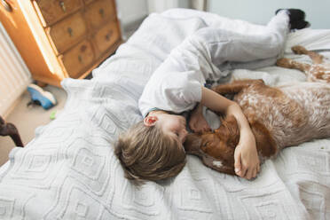 Anhänglicher Junge kuschelt mit Hund auf dem Bett - CAIF28894