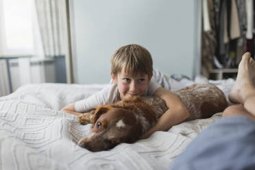 Niedlicher Junge kuschelt mit Hund auf Bett - CAIF28896