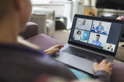 Woman with laptop video chatting with doctors from sofa stock photo