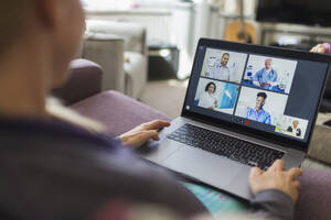 Woman with laptop video chatting with doctors from sofa - CAIF28901