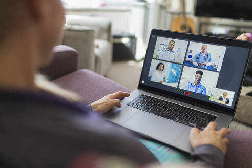 Woman with laptop video chatting with doctors from sofa - CAIF28901