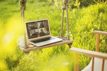 Colleagues video chatting on laptop screen on rustic swing in garden - CAIF28969