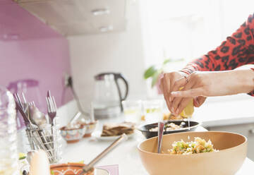 Frau drückt Zitrone über Schüssel mit Essen in der Küche aus - CAIF29043