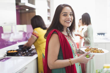Porträt einer glücklichen indischen Frau im Sari, die in der Küche Essen zubereitet - CAIF29046