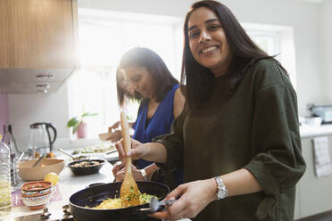 Porträt einer glücklichen indischen Frau, die am Herd in der Küche Essen kocht - CAIF29066