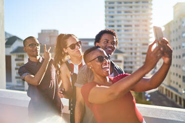 Young friends using smart phone on sunny urban rooftop balcony - CAIF29079