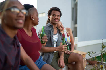 Porträt eines selbstbewussten jungen Mannes, der mit Freunden auf einer Terrasse Bier trinkt - CAIF29083