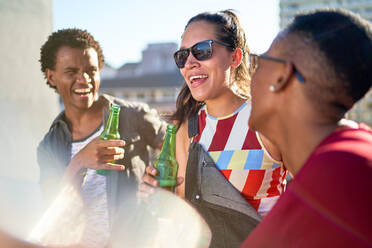 Glückliche junge Freunde trinken Bier auf einem sonnigen Balkon - CAIF29090