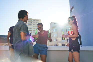 Junge Freunde tanzen und trinken Bier auf einem sonnigen städtischen Dachbalkon - CAIF29092