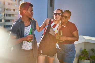 Glückliche junge Freunde trinken Bier auf einem sonnigen städtischen Balkon - CAIF29093