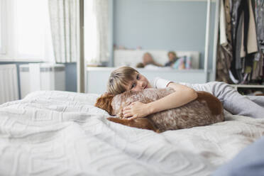 Portrait cute boy cuddling dog on bed - CAIF29108