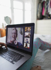Frau mit Laptop im Videochat mit Freunden auf dem Bett - CAIF29109