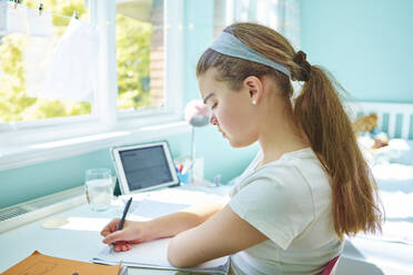 Focused girl doing homework at desk in bedroom - CAIF29115