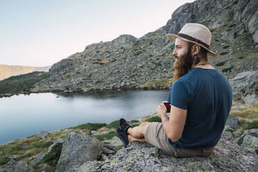 Junger Mann sitzt auf Felsen am See - ADSF06582