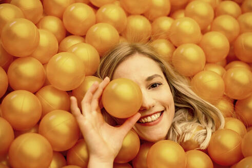 Close-up of smiling beautiful woman lying in orange ball pit - BFRF02271