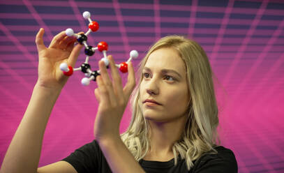 Close-up of female scientist holding molecule model against grid pattern - BFRF02282