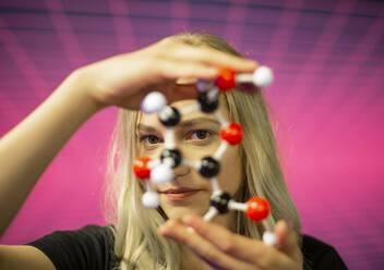 Close-up of young female scientist holding molecule model against grid pattern - BFRF02283