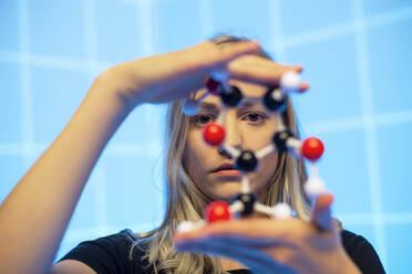 Close-up of young female scientist holding molecule model against blue grid pattern - BFRF02285