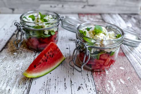 Wassermelonenscheiben und Gläser mit Wassermelonensalat mit Fetakäse, Feldsalat und Minze - SARF04607