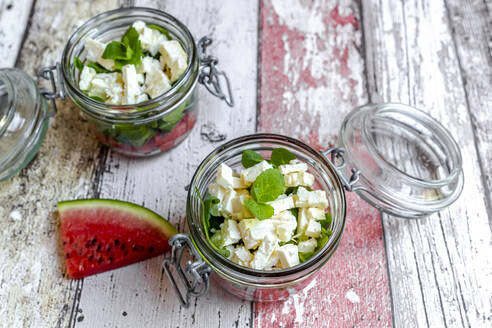 Wassermelonenscheiben und Gläser mit Wassermelonensalat mit Fetakäse, Feldsalat und Minze - SARF04608