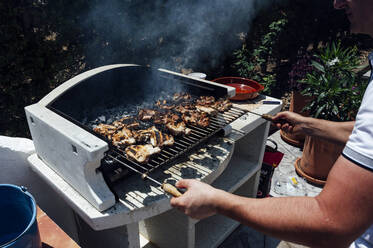 Young man cooking meat on barbecue grill in yard - JCMF01054