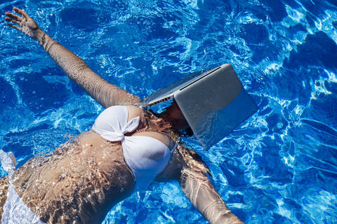 Mid adult woman with laptop on face swimming in pool stock photo