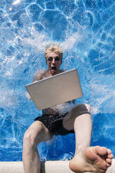 Shocked young man with laptop falling in swimming pool - JCMF01081
