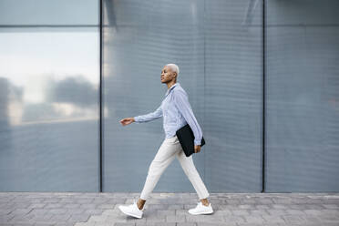 Businesswoman with folder walking against building in city - JRFF04626