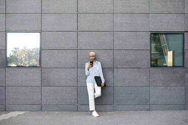 Businesswoman with folder using phone against building in city - JRFF04627