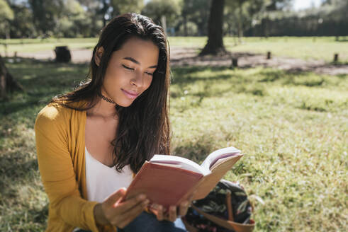 Young woman reading book while sitting on grassy land in park - DSIF00061
