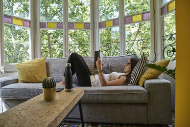 Frau liest ein Buch und entspannt sich auf dem Sofa im Wohnzimmer - VEGF02550