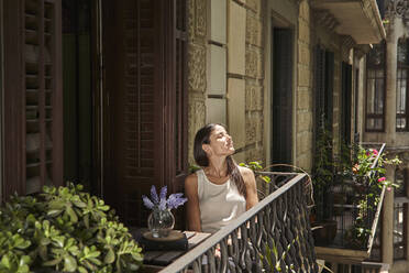 Frau mit geschlossenen Augen entspannt auf dem Balkon - VEGF02553